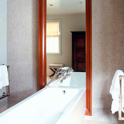 أرضية to ceiling framed mirror rests on the wall behind a modern, sleek, white bath tub