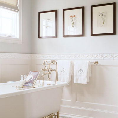три, framed pictures are hung horizontally on the wall above a claw foot tub in a white bathroom