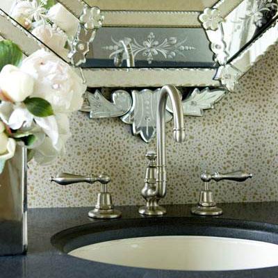 а close up view of a classic bathroom faucet with a decorative patterned mirror behind it and dark countertop