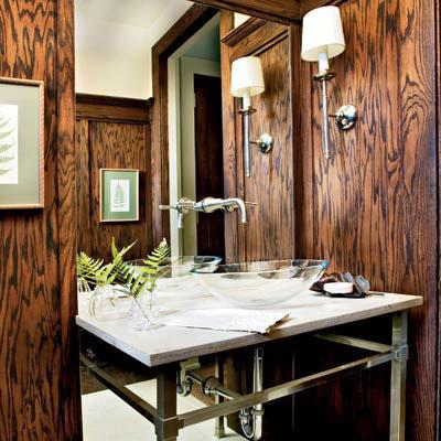 داكن، wood paneling offsets a white marble countertop with a raised glass sink and steel legs in a small bathroom