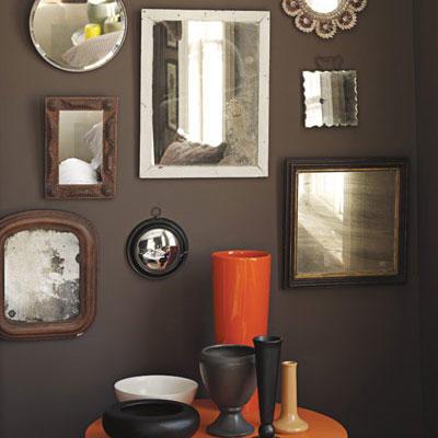 額入り mirrors of various sizes hung on a dark, brown wall with an orange circular table with various sized vases arranged on top