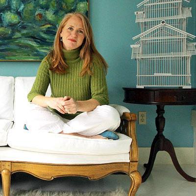 住宅所有者 sitting cross-legged on a white loveseat in front of turquoise walls with a white birdhouse on small end table