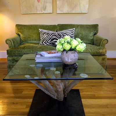 コーヒー table made out of the base of a crepe myrtle with a glass top facing in front of a green couch with a zebra pillow 