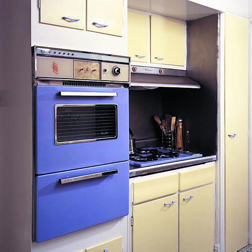 イン this kitchen update, periwinkle paint covers a kitchen oven and stovetop while the cabinets’ doors are painted a pale yellow color with rest covered in creamy white.