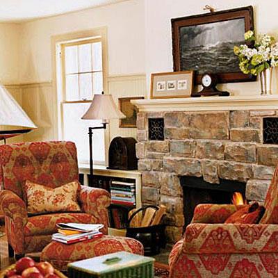 Голям, natural stones around the hearth update this fireplace's style while red and tan velvet fabric decorates the arm chairs that are placed on either side.