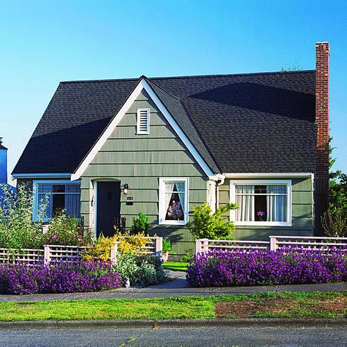 明るい purple and yellow flowers border the front sidewalk with a low, white fence behind them