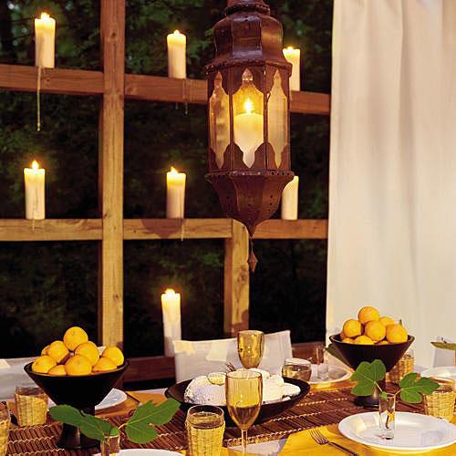 أبيض candles are placed on the wooden ledges surrounding the deck with a table decorated with lemons in bowls, a hanging lantern, white plates and wine glasses