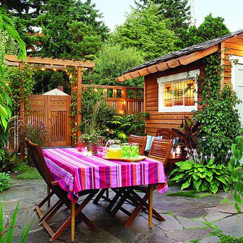 ярък and colorful backyard with a striped tablecloth over an outdoor table with a wooden garden shed, in the background