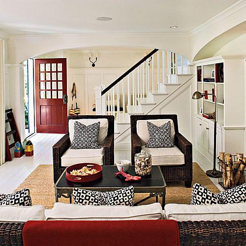 白 walls and cabinets in the living room highlight black and white patterned pillows on the arm chairs, with a red throw set behind the couch