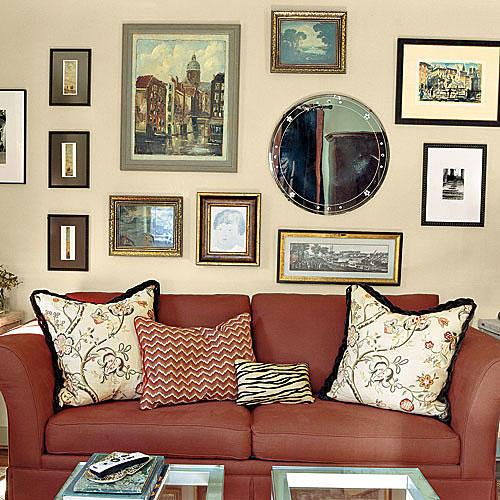 家族 room wall with gallery layout of framed prints, paintings and mirrors hung over a red couch with pillows