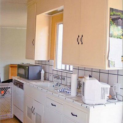 مطبخ with peach cupboards above the sink and white cupboards below with white tile backsplash and tile counters