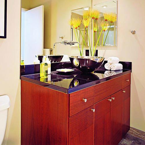 а stainless steel vessel sink sits on top of black granite sink counter top with cherry wood kitchen-cabinet base below in this teen's bathroom