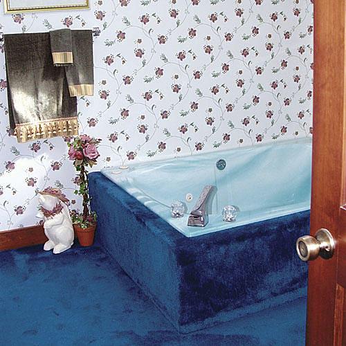 ярък blue carpet runs up along the sides of the tub and outdated wallpaper with small flowers off-sets this dated master bathroom