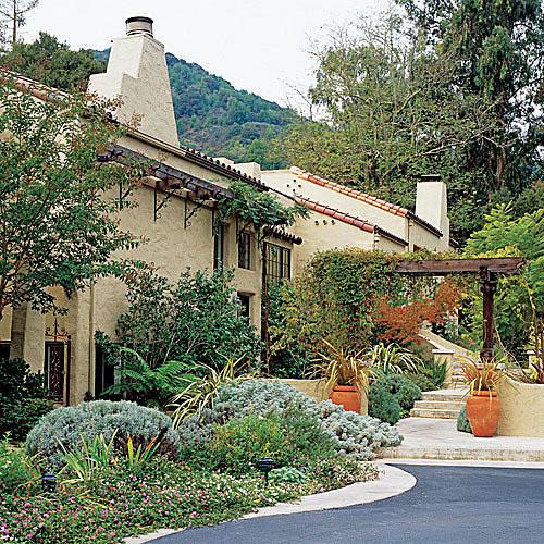 буйни, planting beds, bushes and container plants line the front of the Mediterranean style home