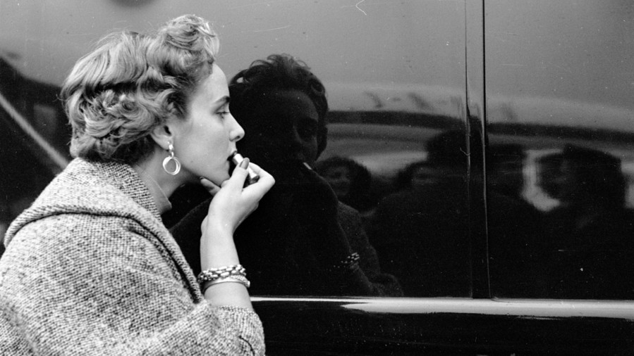 女性 applying lipstick using car reflection